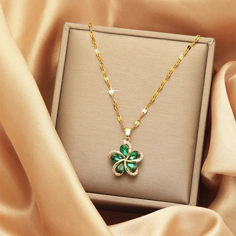 Elegant gold necklace with a vibrant green flower pendant featuring sparkling clear accents, presented in a beige jewelry box against a luxurious gold satin fabric. Floral jewelry gift for women