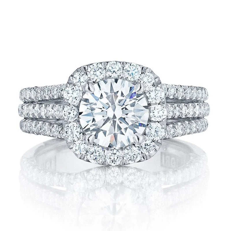 A stunning white gold engagement ring featuring a large, brilliant-cut round surrounded by a sparkling halo of smaller, accompanied by two delicate pave bands, displayed on a reflective white surface, symbolizing a timeless and elegant commitment.
