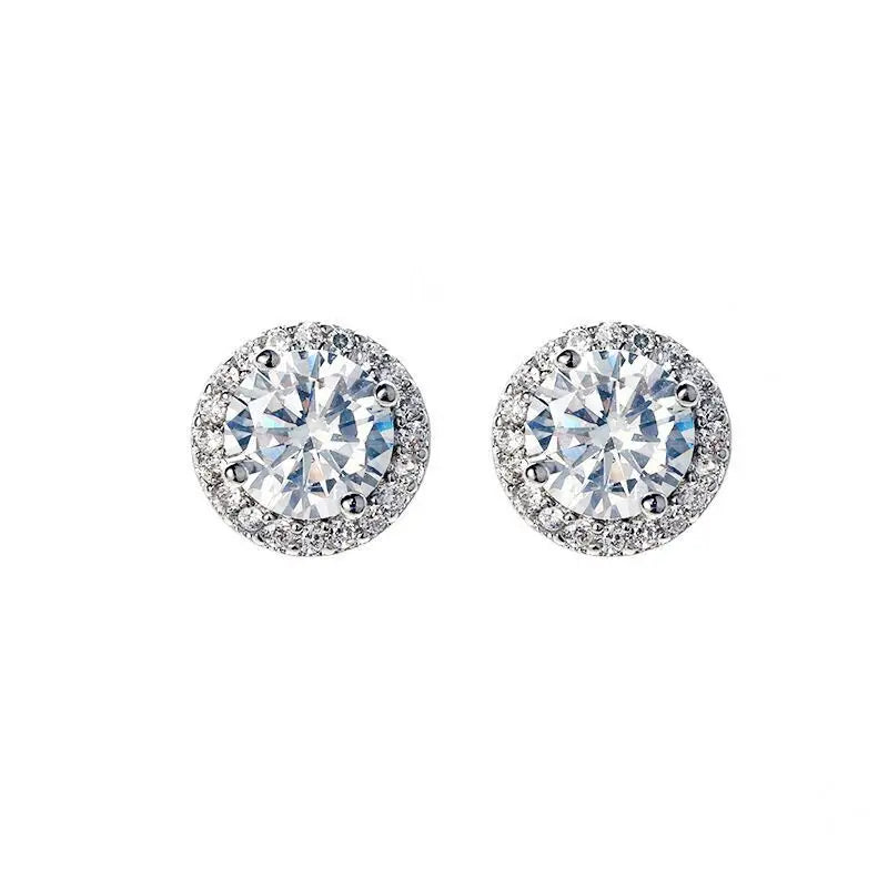 A pair of dazzling round stud earrings featuring a large, brilliant-cut center stone surrounded by a halo of smaller sparkling stones, presented against a plain white background, perfect for adding elegance to any occasion.